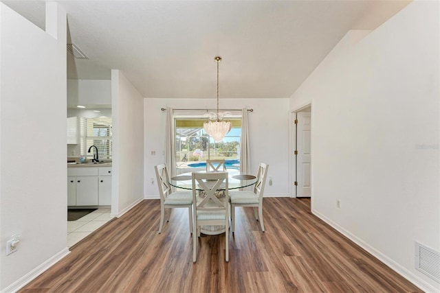 dining area featuring sink, light hardwood / wood-style flooring, vaulted ceiling, and an inviting chandelier