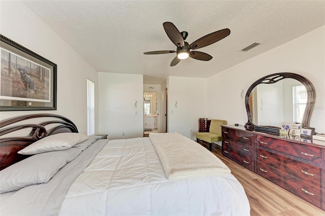 bedroom featuring a textured ceiling, light hardwood / wood-style floors, ensuite bath, and ceiling fan