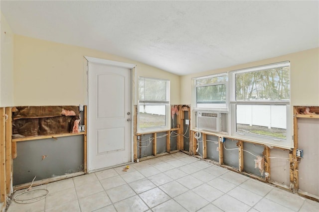 misc room with lofted ceiling, cooling unit, light tile patterned floors, and a textured ceiling