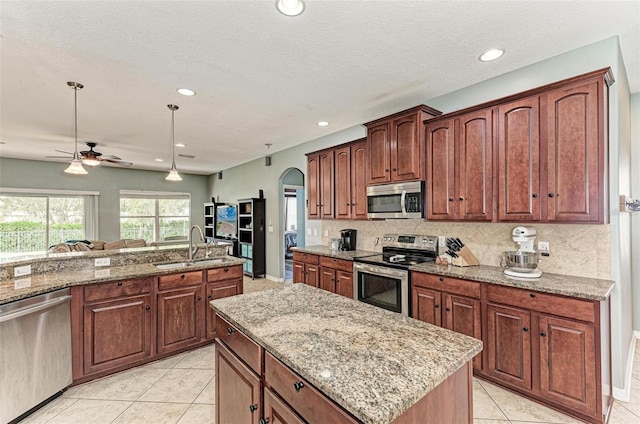 kitchen with stainless steel appliances, a center island, light stone countertops, pendant lighting, and sink