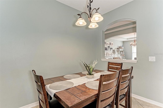 tiled dining area featuring a raised ceiling and a chandelier