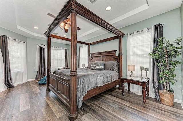 bedroom with wood-type flooring, a textured ceiling, ceiling fan, and a tray ceiling