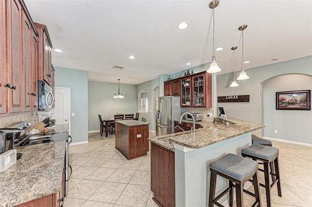 kitchen featuring appliances with stainless steel finishes, a breakfast bar area, hanging light fixtures, kitchen peninsula, and light stone countertops