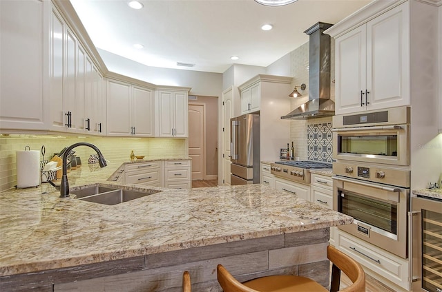 kitchen featuring beverage cooler, appliances with stainless steel finishes, wall chimney exhaust hood, sink, and a breakfast bar