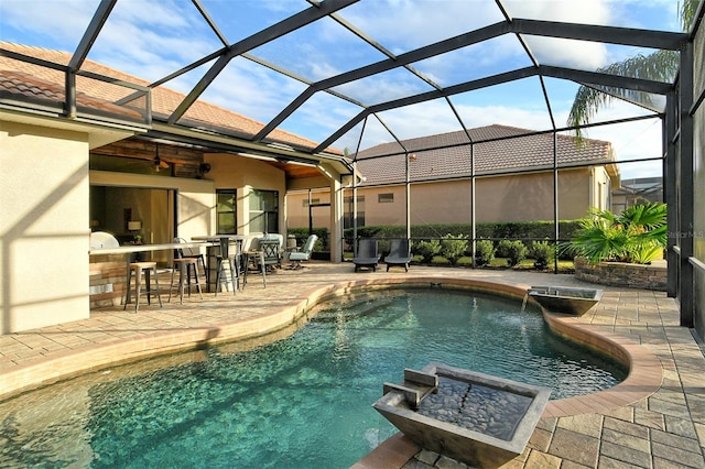 view of pool with an outdoor kitchen, glass enclosure, an outdoor bar, and a patio