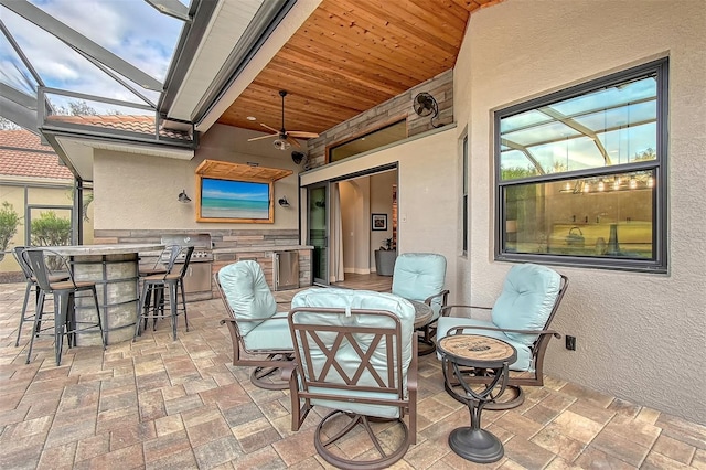 view of patio / terrace featuring ceiling fan, exterior kitchen, an outdoor bar, and a lanai