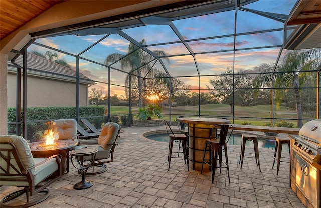 patio terrace at dusk with a lanai, exterior kitchen, and a fire pit