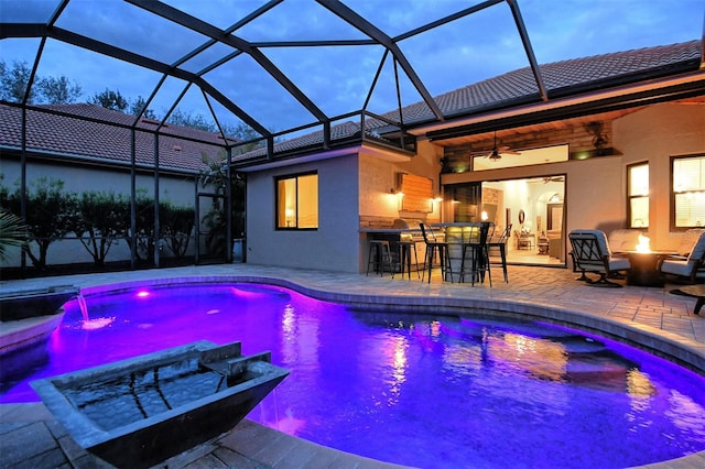 pool at dusk with a patio area, a lanai, a bar, and a fire pit