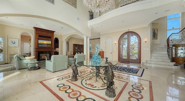 entrance foyer featuring a towering ceiling, crown molding, ornate columns, and french doors