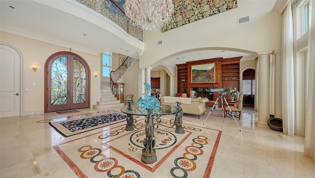 entrance foyer featuring french doors, a towering ceiling, crown molding, and ornate columns