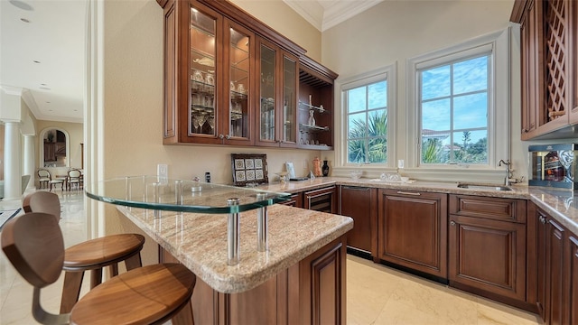 kitchen with kitchen peninsula, sink, light stone countertops, a breakfast bar area, and ornamental molding