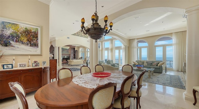 dining area featuring decorative columns, crown molding, a water view, and an inviting chandelier