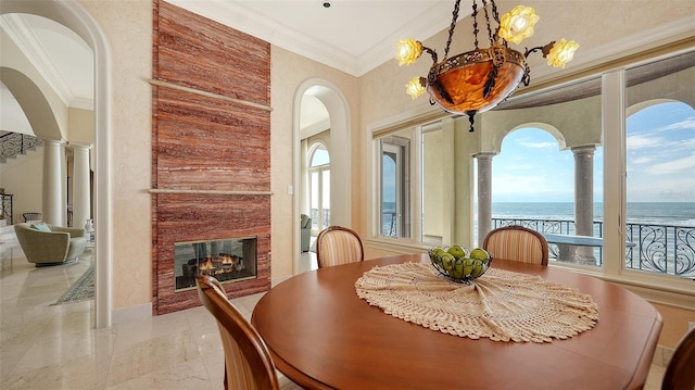 dining space with a fireplace, ornamental molding, a water view, and decorative columns