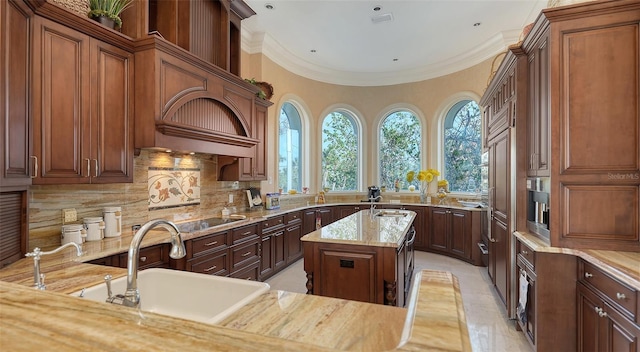 kitchen featuring crown molding, sink, backsplash, and an island with sink