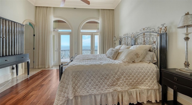 bedroom featuring hardwood / wood-style floors, ceiling fan, access to exterior, ornamental molding, and a water view