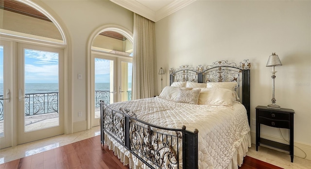 bedroom with access to exterior, hardwood / wood-style floors, ornamental molding, a water view, and french doors