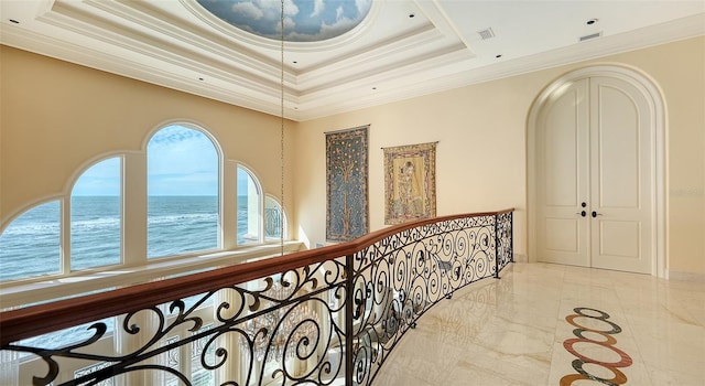 corridor with crown molding, a water view, and a tray ceiling