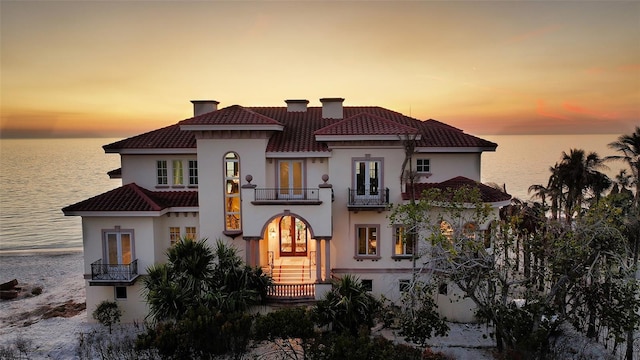 mediterranean / spanish-style home featuring a chimney, a water view, a balcony, and stucco siding