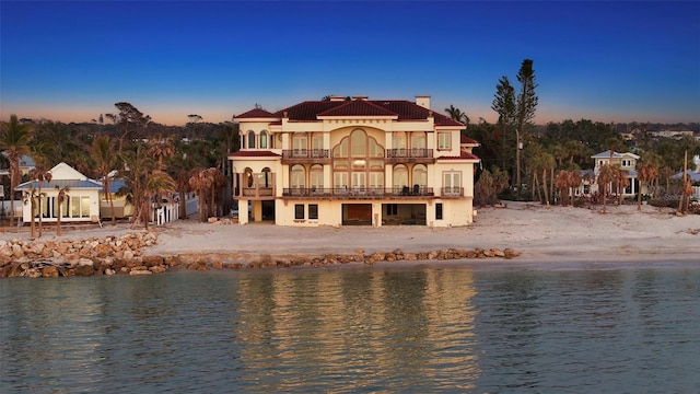 rear view of house featuring a water view, a balcony, a chimney, and stucco siding