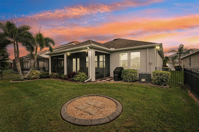 back house at dusk with a lawn, central air condition unit, and a sunroom