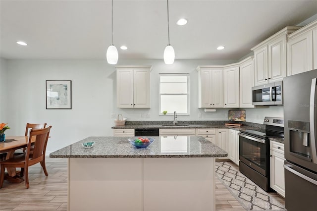 kitchen with white cabinets, appliances with stainless steel finishes, a center island, sink, and hanging light fixtures