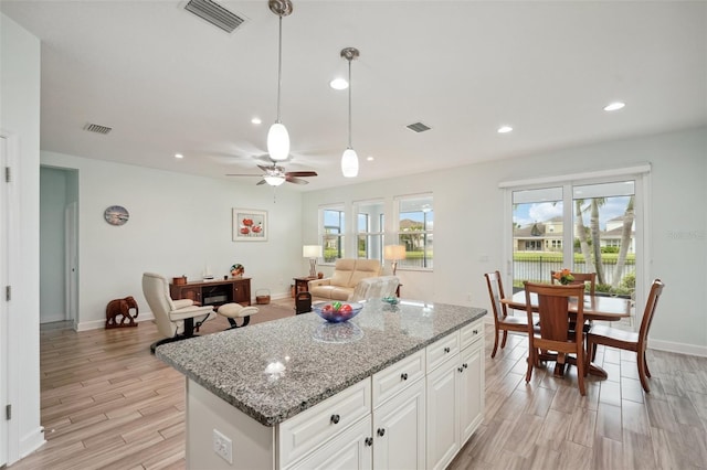 kitchen featuring ceiling fan, decorative light fixtures, white cabinets, light stone counters, and a center island