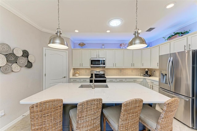 kitchen featuring decorative light fixtures, a center island with sink, tasteful backsplash, white cabinets, and appliances with stainless steel finishes