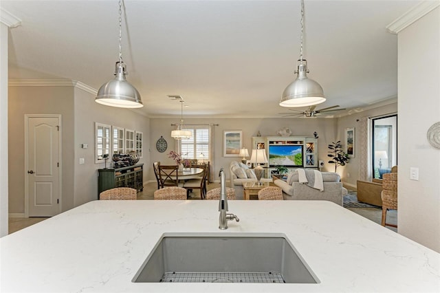 kitchen with sink, hanging light fixtures, crown molding, and light stone countertops