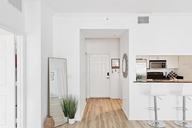 kitchen featuring a kitchen breakfast bar, stainless steel appliances, crown molding, and light hardwood / wood-style flooring