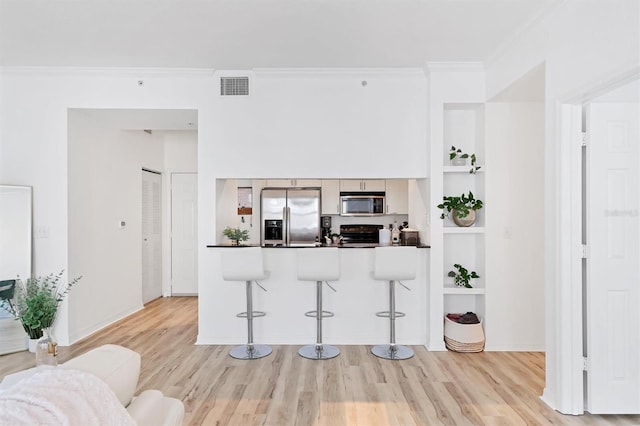 kitchen with light hardwood / wood-style floors, kitchen peninsula, a breakfast bar area, appliances with stainless steel finishes, and ornamental molding