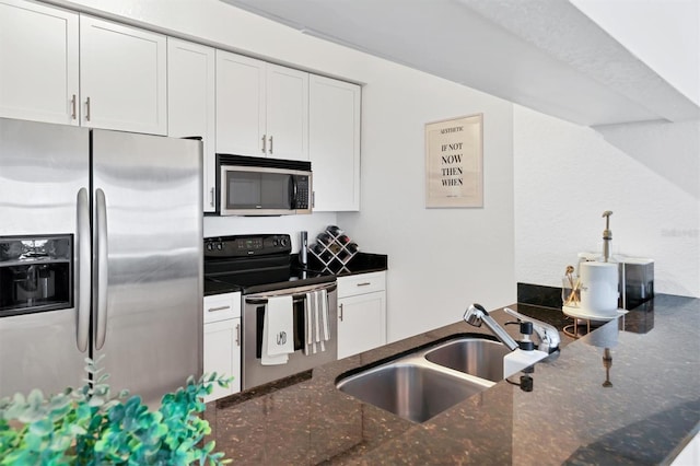 kitchen with kitchen peninsula, sink, white cabinetry, appliances with stainless steel finishes, and dark stone counters