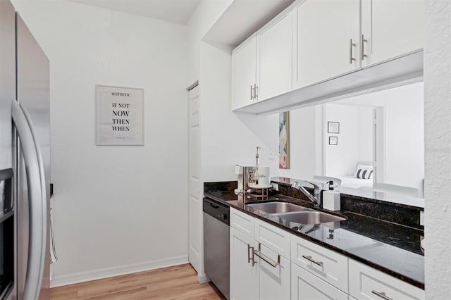 kitchen with dark stone countertops, sink, white cabinetry, light wood-type flooring, and stainless steel appliances