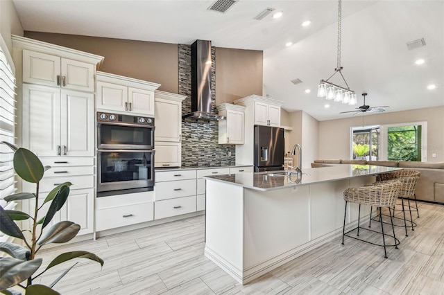 kitchen with lofted ceiling, wall chimney exhaust hood, stainless steel appliances, backsplash, and ceiling fan