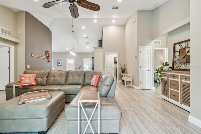 living room featuring ceiling fan, a high ceiling, and light hardwood / wood-style flooring