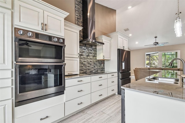 kitchen with appliances with stainless steel finishes, tasteful backsplash, wall chimney range hood, white cabinets, and sink