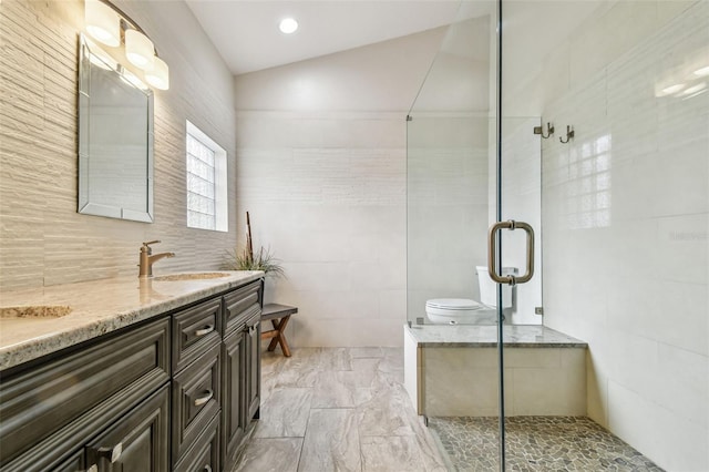 bathroom with tile walls, vaulted ceiling, a shower with door, and vanity