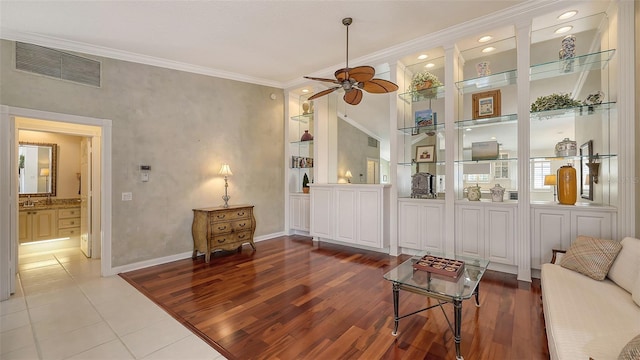 living room featuring built in shelves, ceiling fan, crown molding, and light hardwood / wood-style flooring