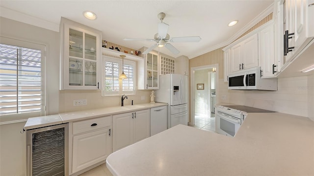 kitchen with sink, white cabinets, beverage cooler, and white appliances