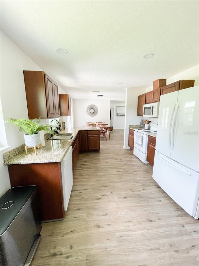 kitchen with white appliances, kitchen peninsula, sink, and light wood-type flooring