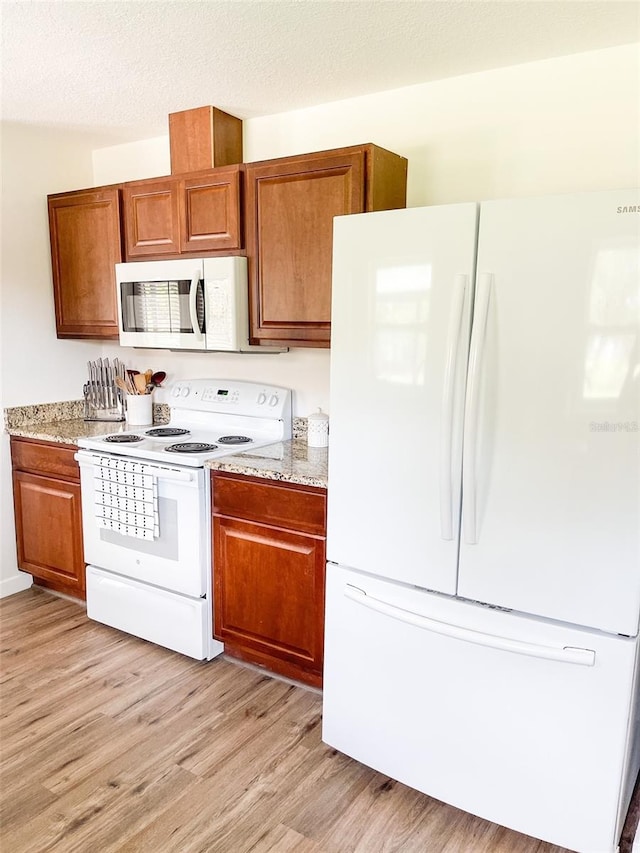 kitchen with light stone counters, white appliances, a textured ceiling, and light hardwood / wood-style flooring