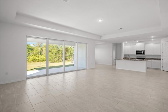 unfurnished living room featuring sink, a raised ceiling, and light tile patterned floors