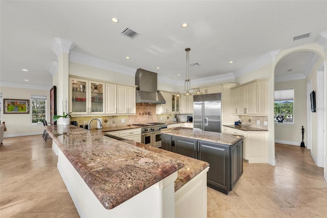 kitchen featuring pendant lighting, wall chimney range hood, a large island, dark stone countertops, and premium appliances