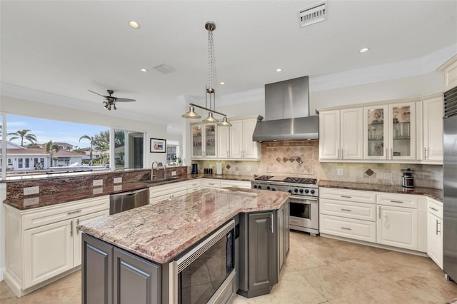 kitchen with stainless steel appliances, hanging light fixtures, wall chimney range hood, and dark stone counters