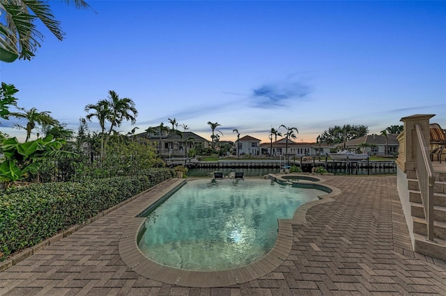 pool at dusk with an in ground hot tub and a patio