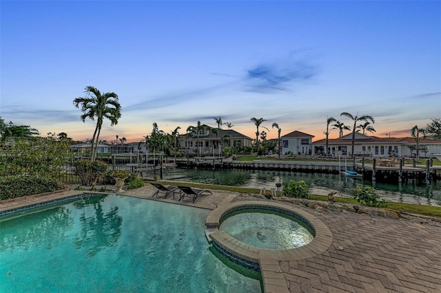 pool at dusk with an in ground hot tub and a water view