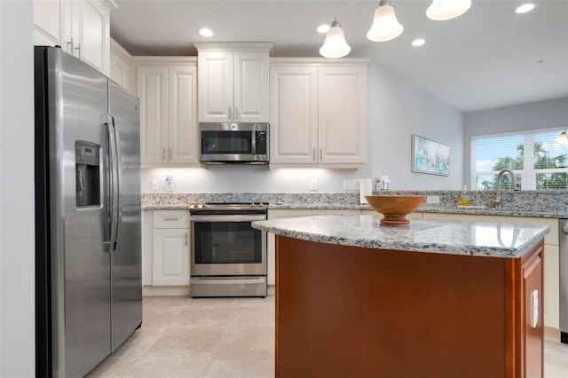 kitchen with decorative light fixtures, white cabinets, light stone counters, and appliances with stainless steel finishes