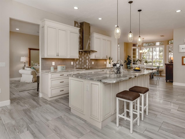 kitchen featuring pendant lighting, wall chimney exhaust hood, white cabinetry, a large island, and a breakfast bar area