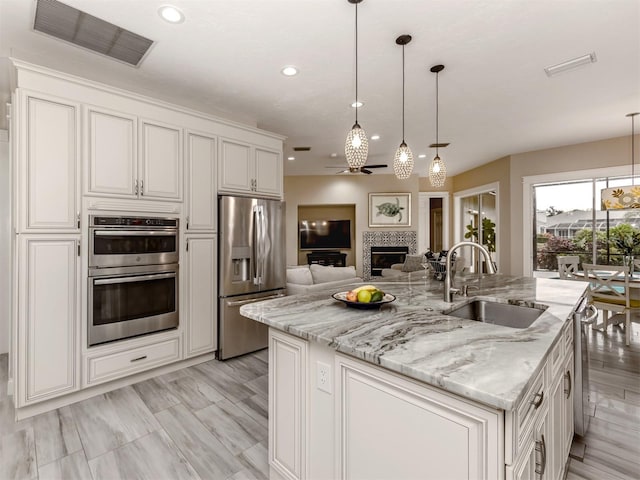 kitchen with sink, a kitchen island with sink, decorative light fixtures, and stainless steel appliances