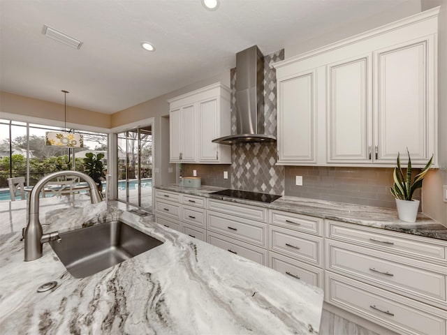 kitchen featuring sink, decorative light fixtures, white cabinets, light stone counters, and wall chimney exhaust hood