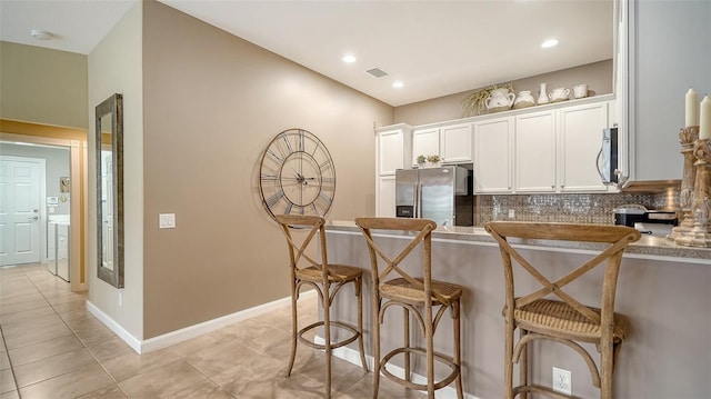 kitchen with white cabinetry, decorative backsplash, stainless steel fridge, a breakfast bar, and light tile patterned floors